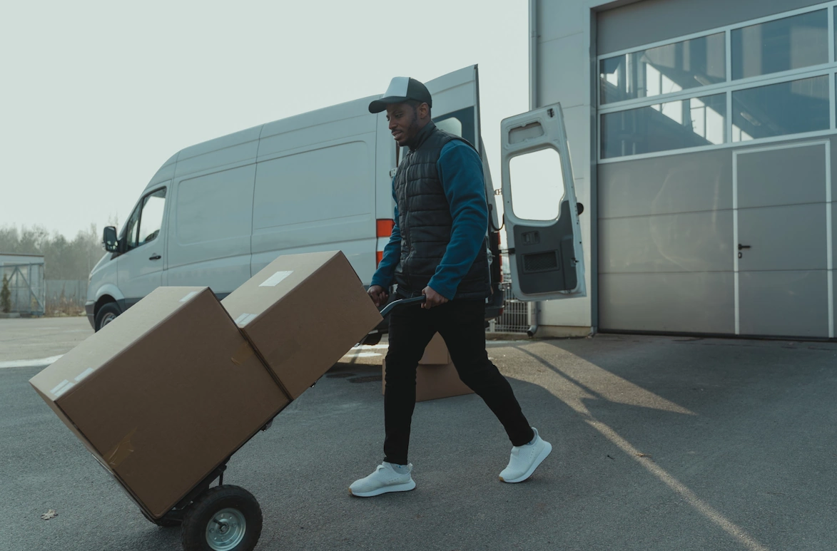 a person who's pushing some packages from the middle to the left and a business vehicle behind him