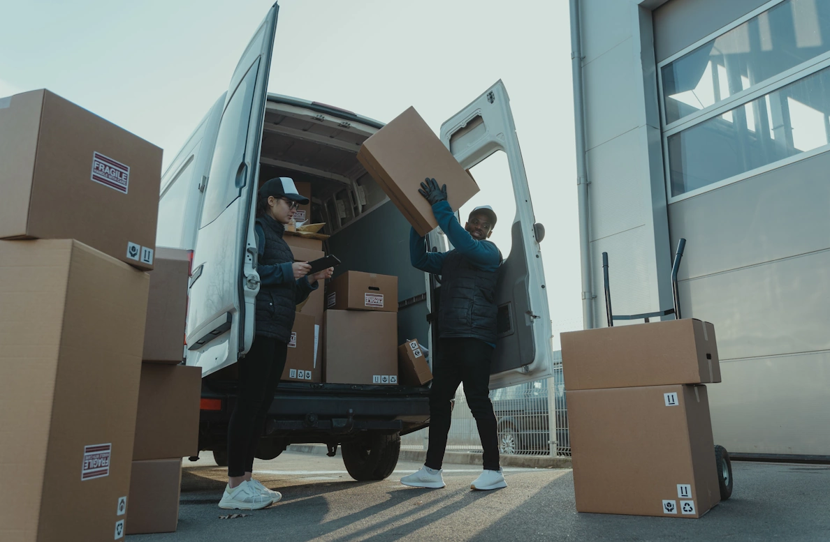 two person picking up packages from the back of a business vehicle